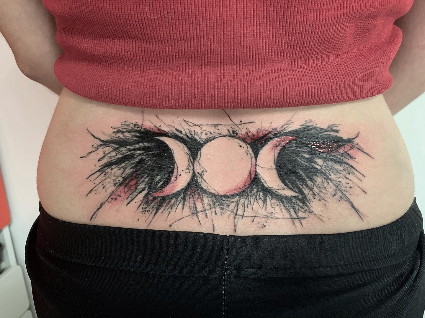 Tattoo of three moon phases on lower back, featuring splashes of black and red ink